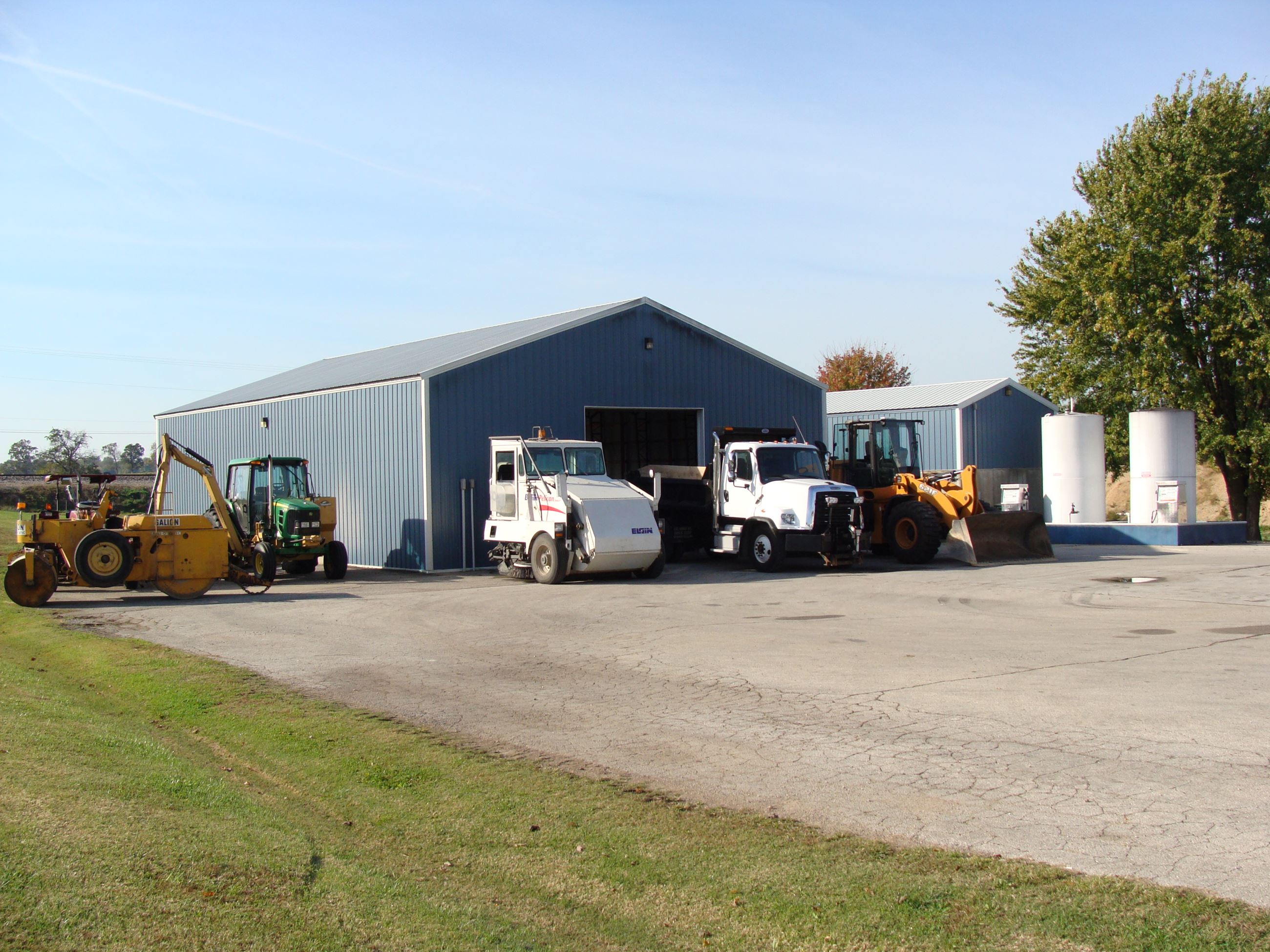 Street Department building with yellow bull dozers, white trucks and a green John Deere tractor